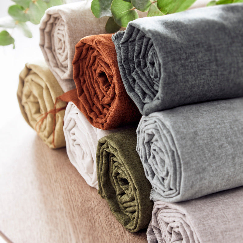 Stack of folded fabric rolls in various colors on a wooden surface with green leaves in the background.