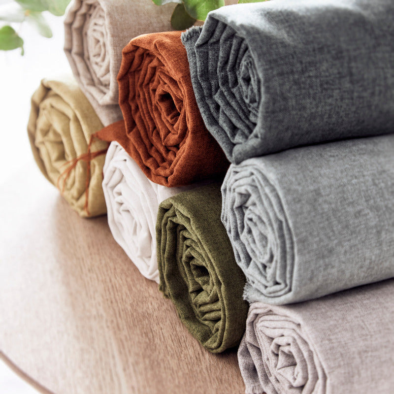 Stack of folded fabric rolls in various colors on a wooden surface with green leaves in the background.