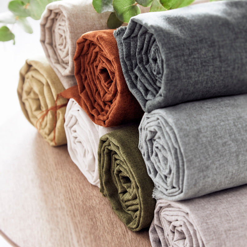 Stack of folded fabric rolls in various colors on a wooden surface with green leaves in the background.