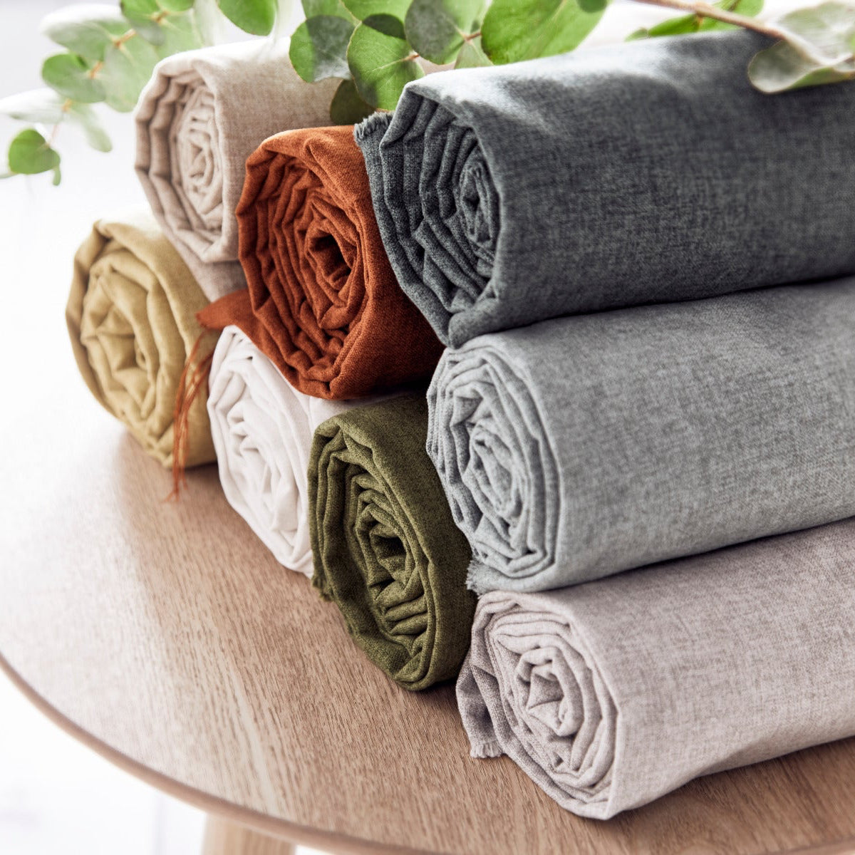 Rolled-up fabric samples in various colors on a wooden surface with greenery in the background