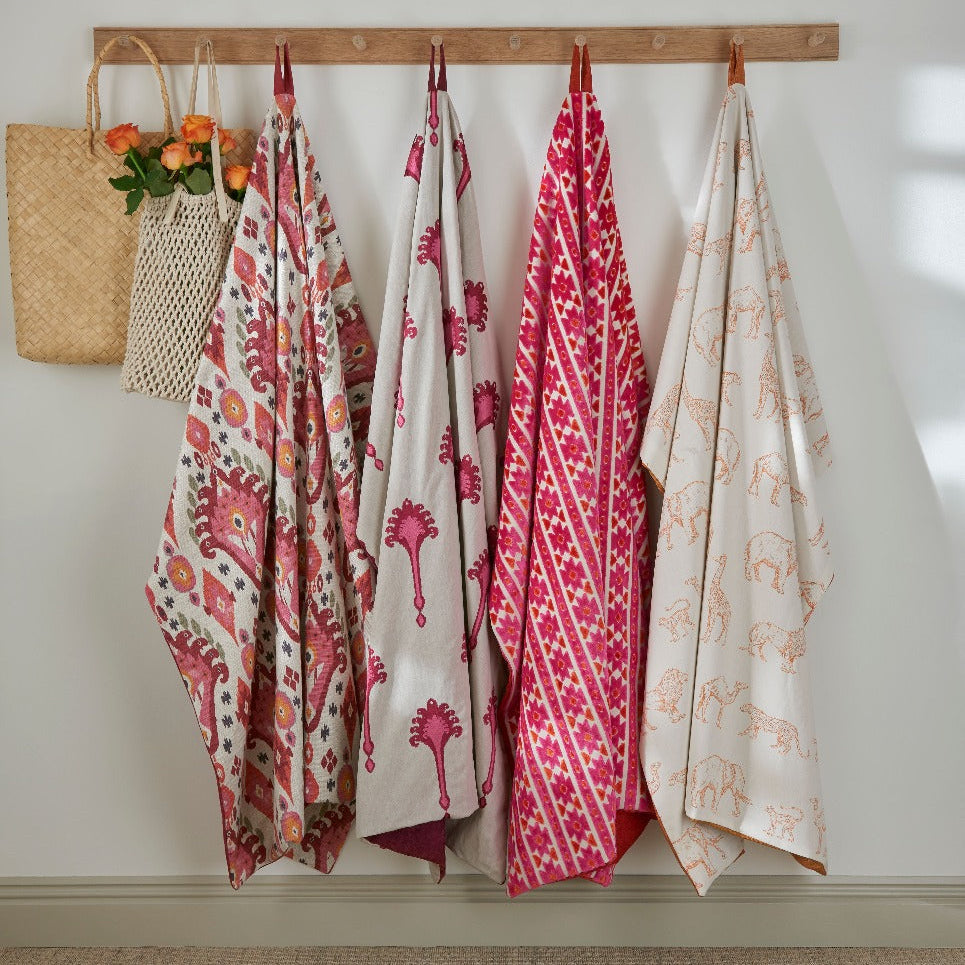 Colorful patterned fabrics hanging on a wooden rack against a white wall.