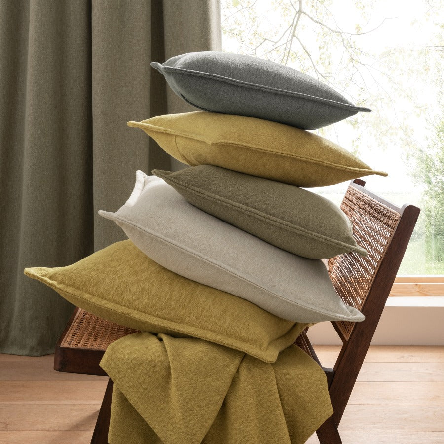 Stack of colorful pillows and a blanket on a wooden chair by a window.