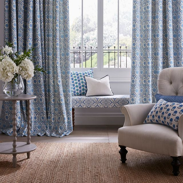 Living room with blue patterned curtains, a beige armchair, and a small table with flowers.