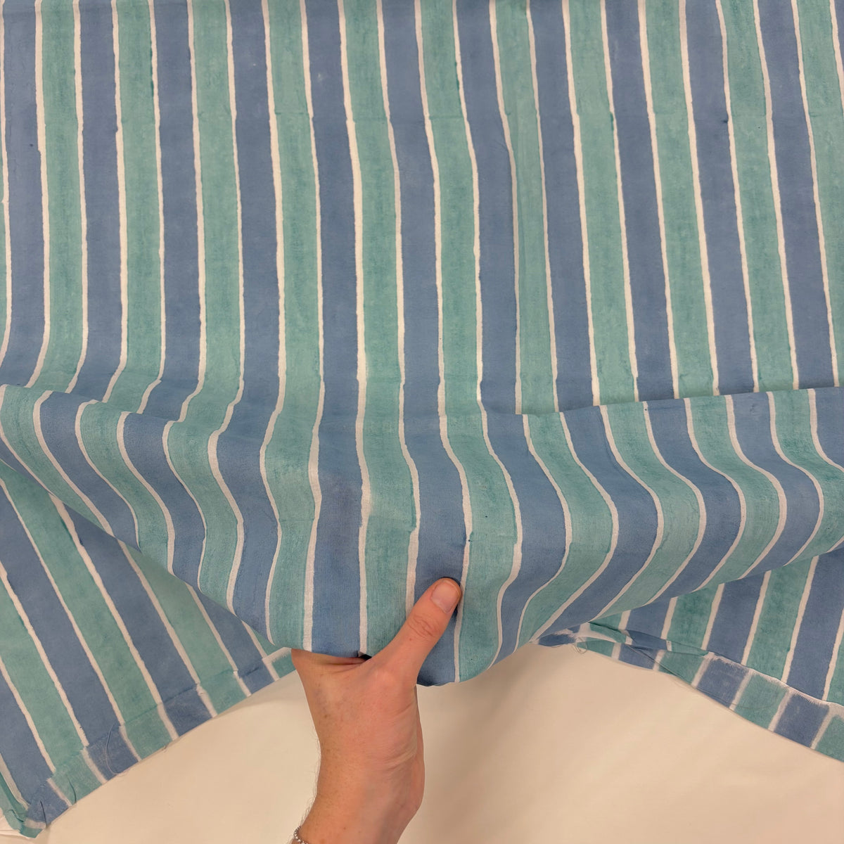 Blue Ocean Stripe Indian Print Cotton Fabric, with hand for scale, lightweight soft cotton with a traditional handcrafted Indian tartan check pattern.