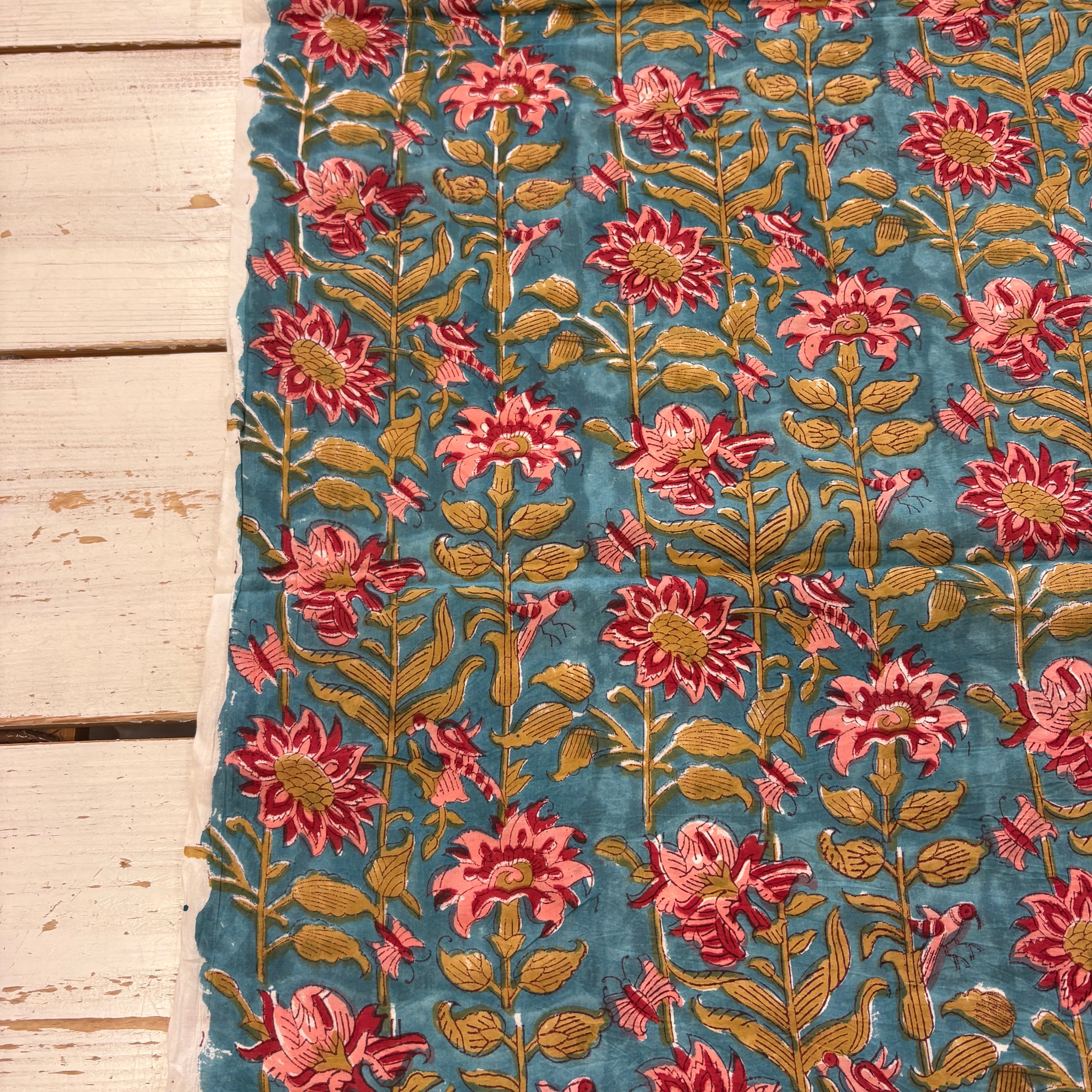 A close-up of a blue fabric with an embroidered floral pattern in pink, red, and green, laid flat on a light-colored wooden surface.