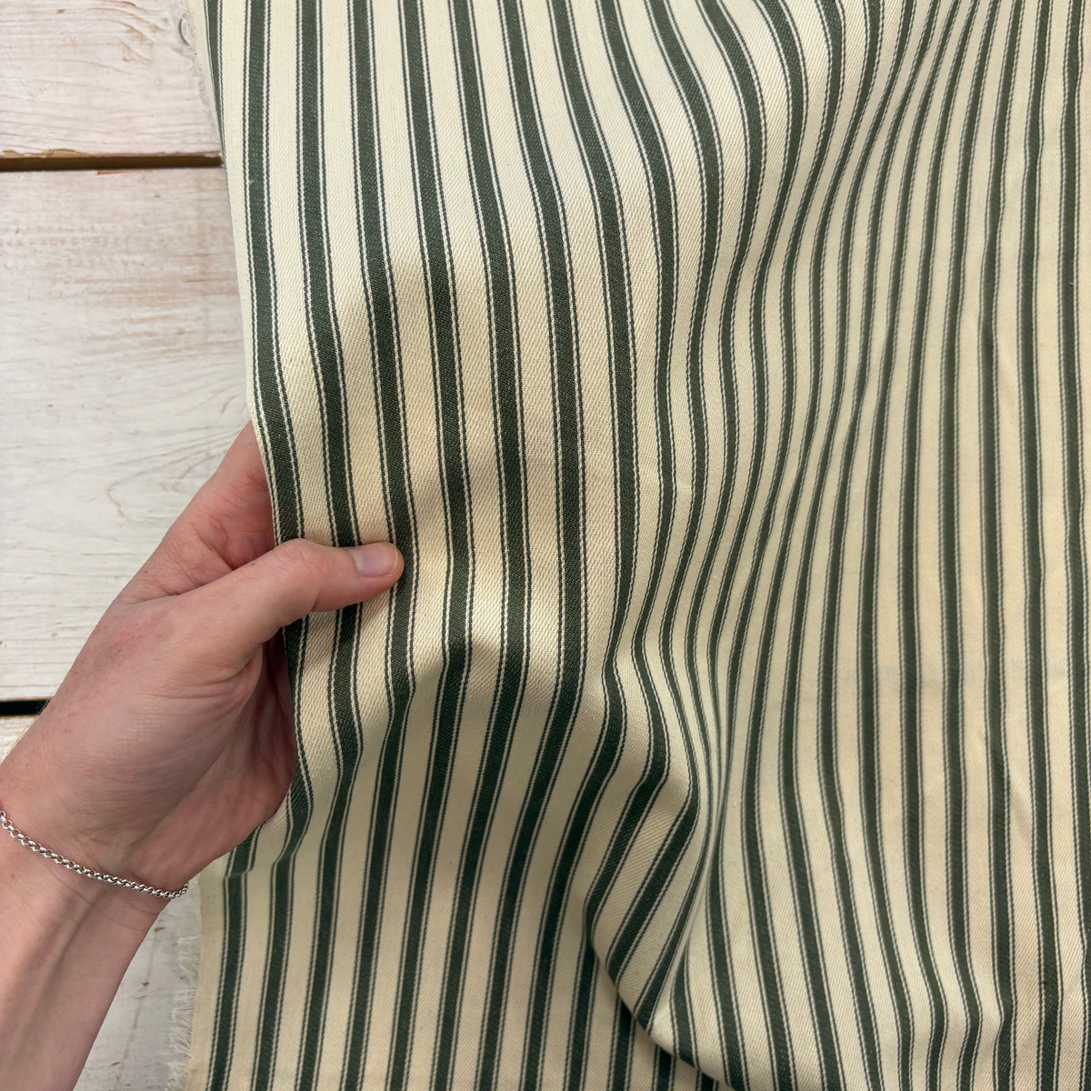 Classic forest green cotton ticking fabric with traditional stripes with hand for scale, ideal for cushions, tablecloths, table runners, lampshades, home furnishings and DIY craft projects. 