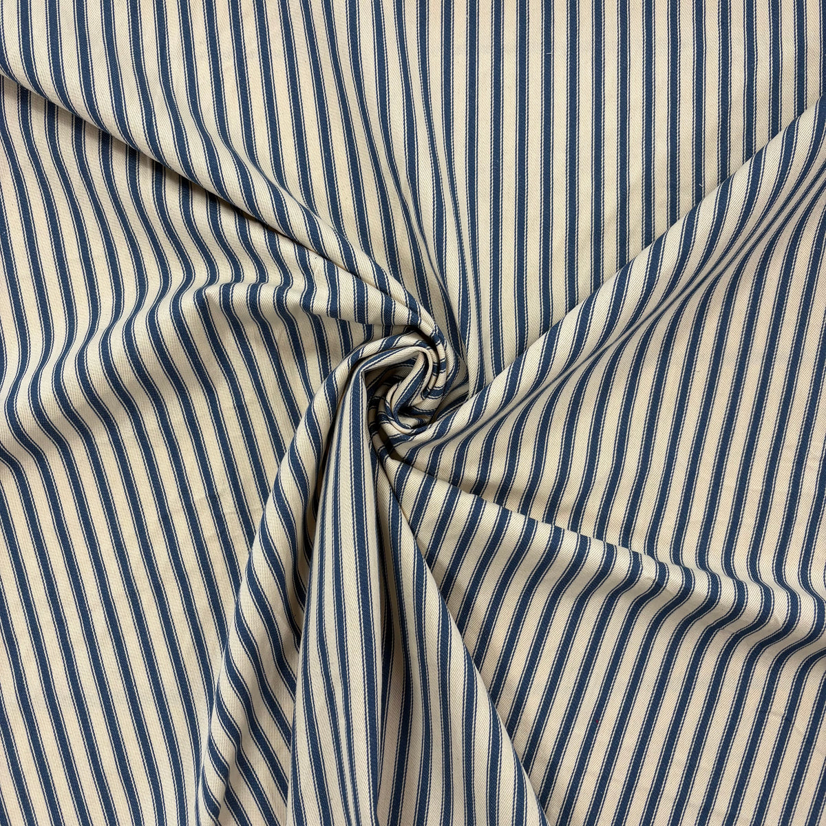 Classic navy blue cotton ticking fabric with traditional stripes and a soft handle twisted to show drape, ideal for cushions, tablecloths, table runners, lampshades, home furnishings and DIY craft projects. Timeless striped cotton fabric for contemporary and country style interiors.