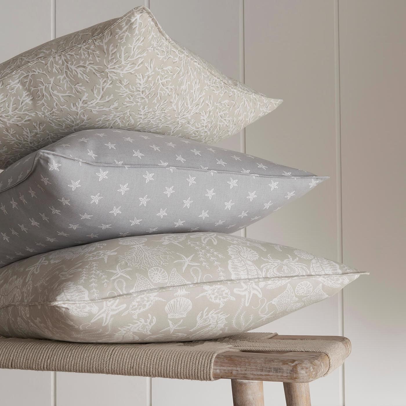 Three patterned pillows stacked on a wooden stool against a light gray wall.