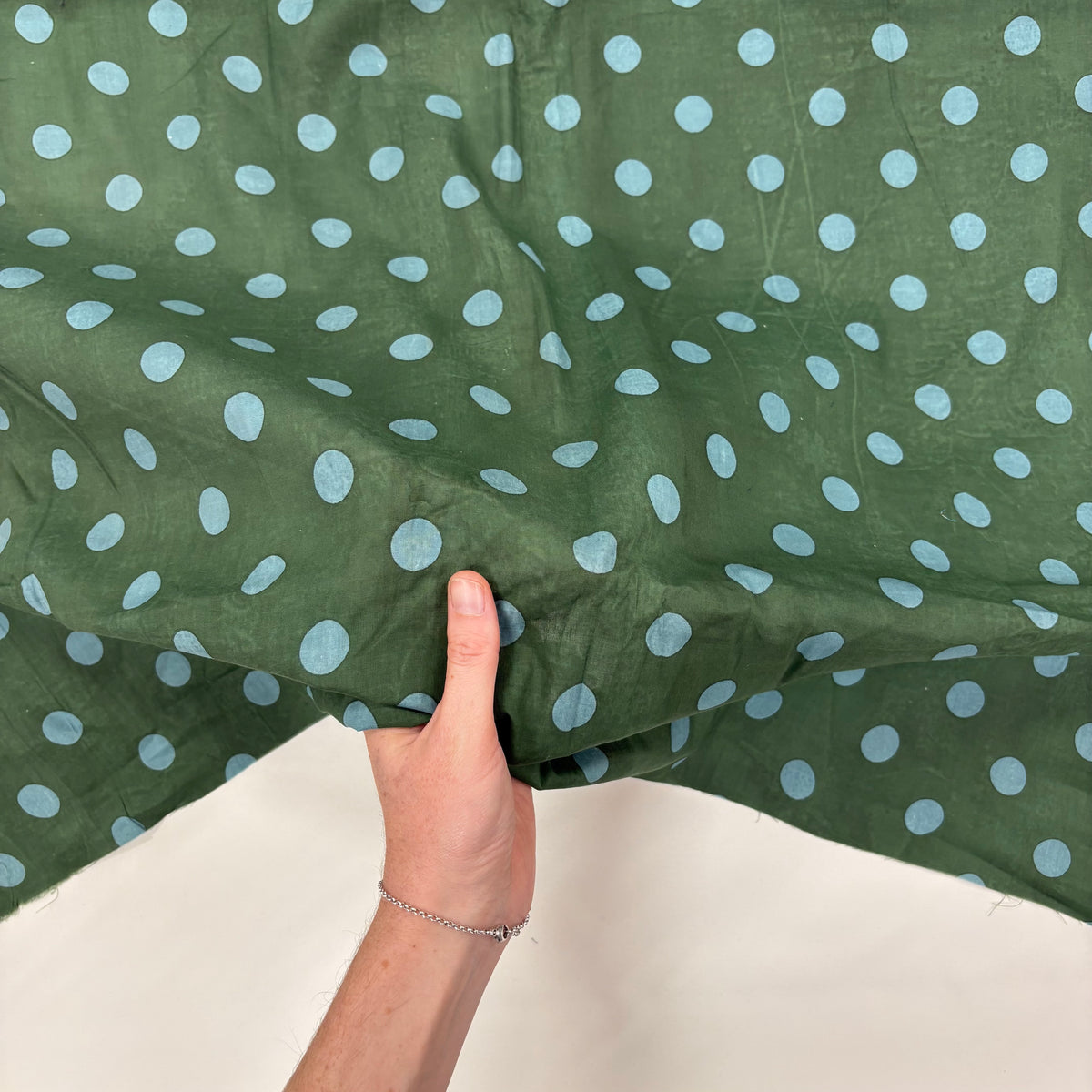 Forest Green Spotty Indian Print Cotton Fabric with hand for scale, lightweight 100gsm printed cotton for dressmaking, handmade gifts, crafts and soft furnishings, handcrafted using traditional Indian printing techniques.