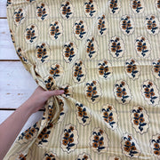 A hand holding a cream-colored cotton fabric with a vertical stripe pattern and a repeating block print of floral motifs inside decorative cartouches.