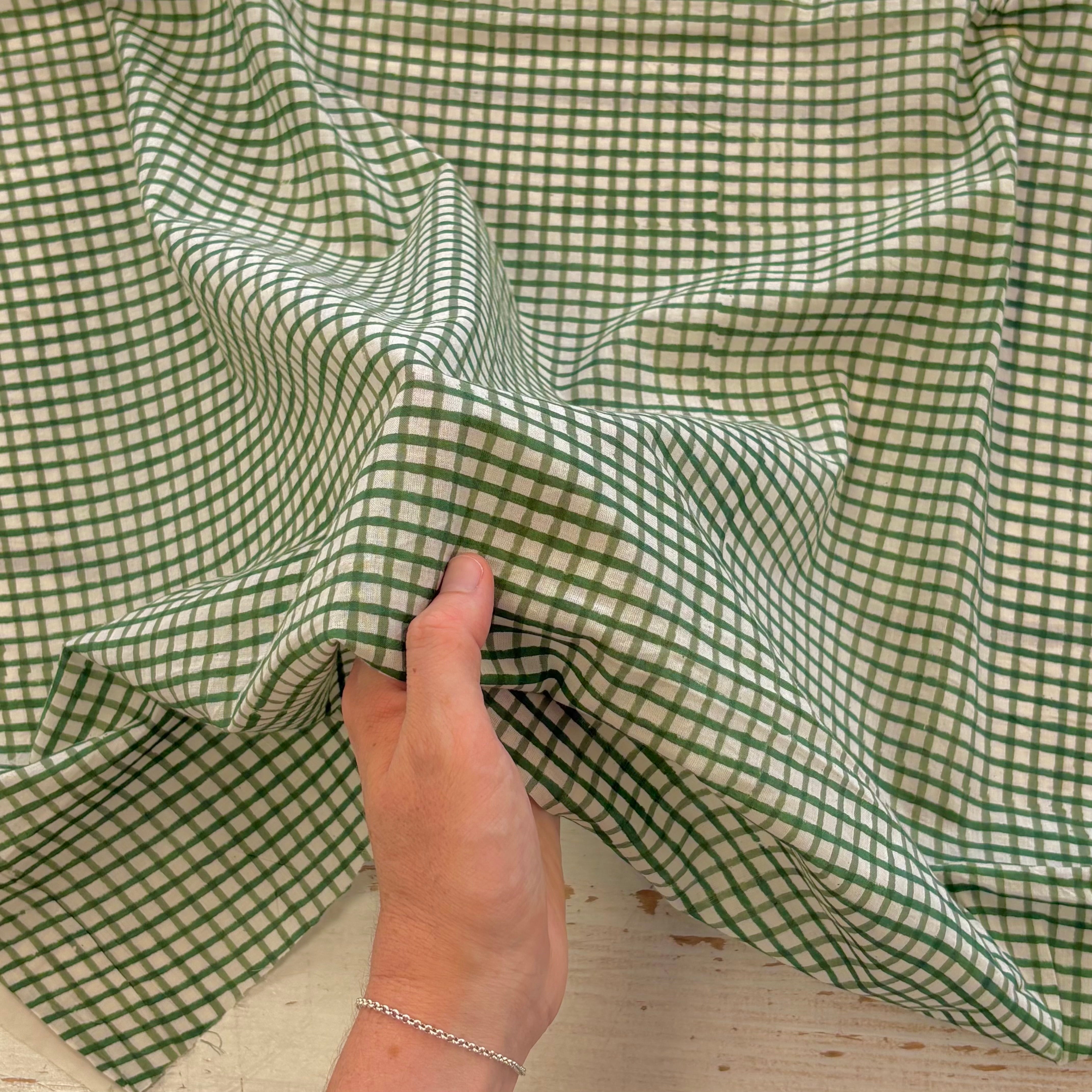 A close-up of a green and white gingham fabric being held by a hand, showing its texture and pattern.