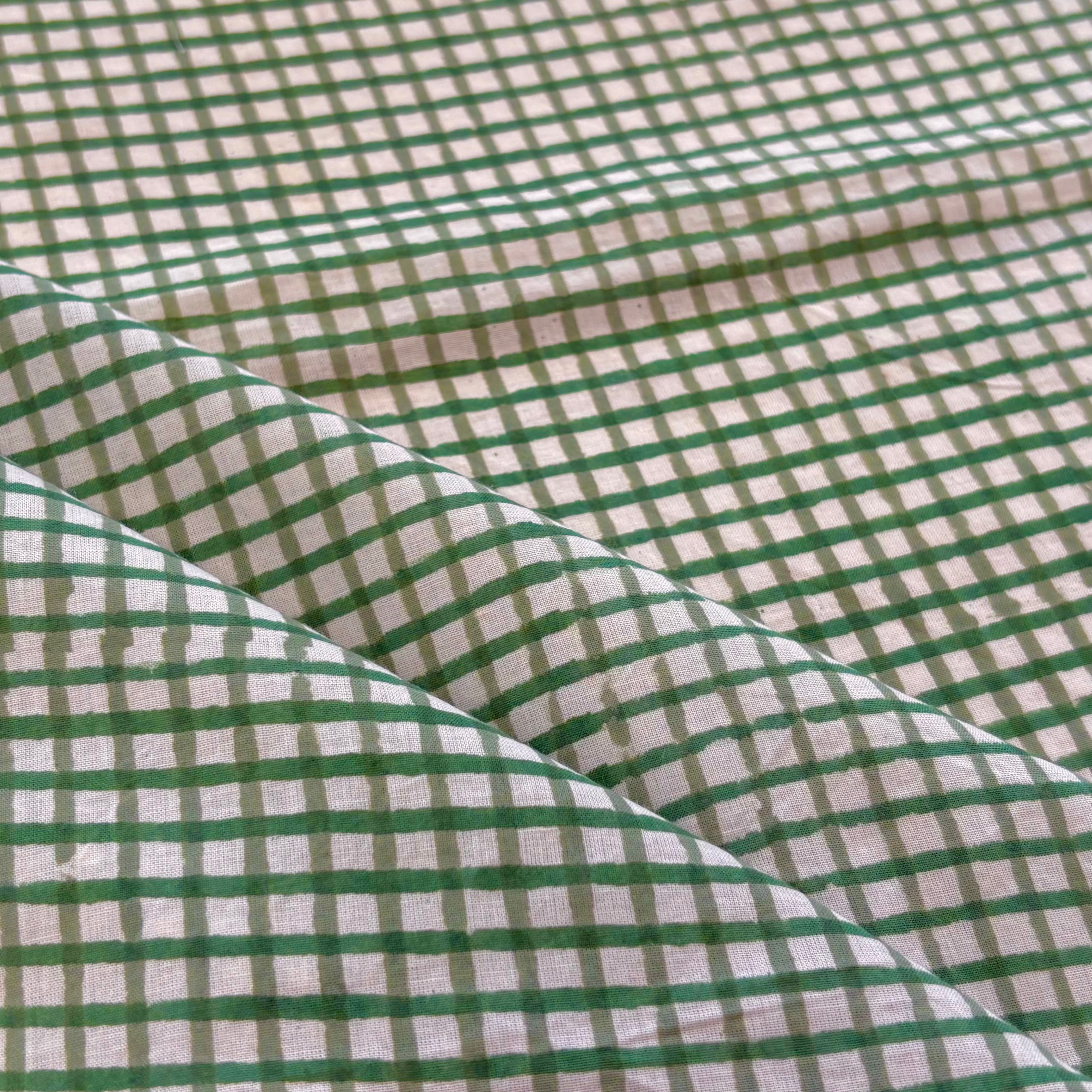Green and white gingham checkered fabric with soft folds showing its texture and pattern.
