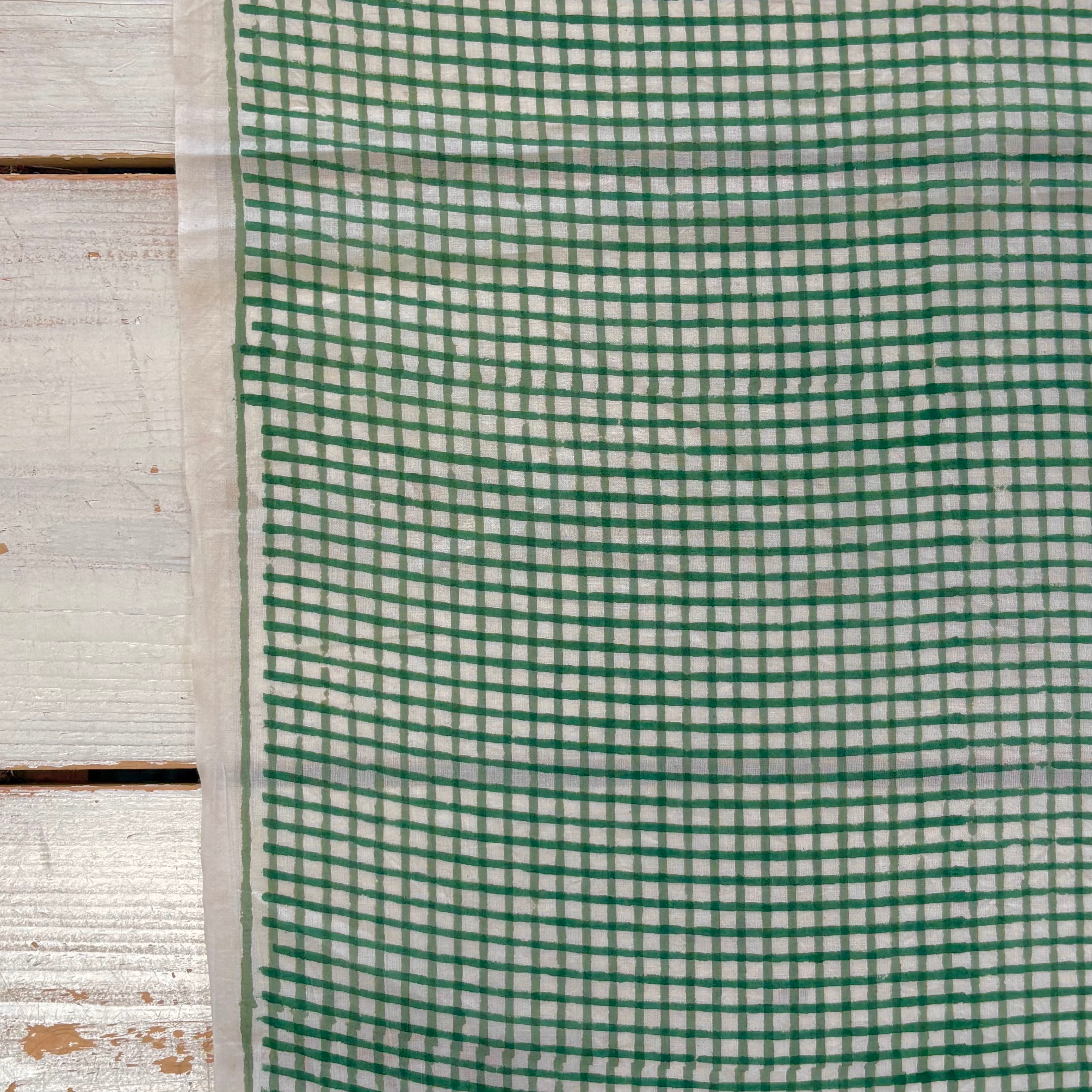 A close-up of a green and white gingham checkered fabric,  laid flat on a rustic white wooden surface.