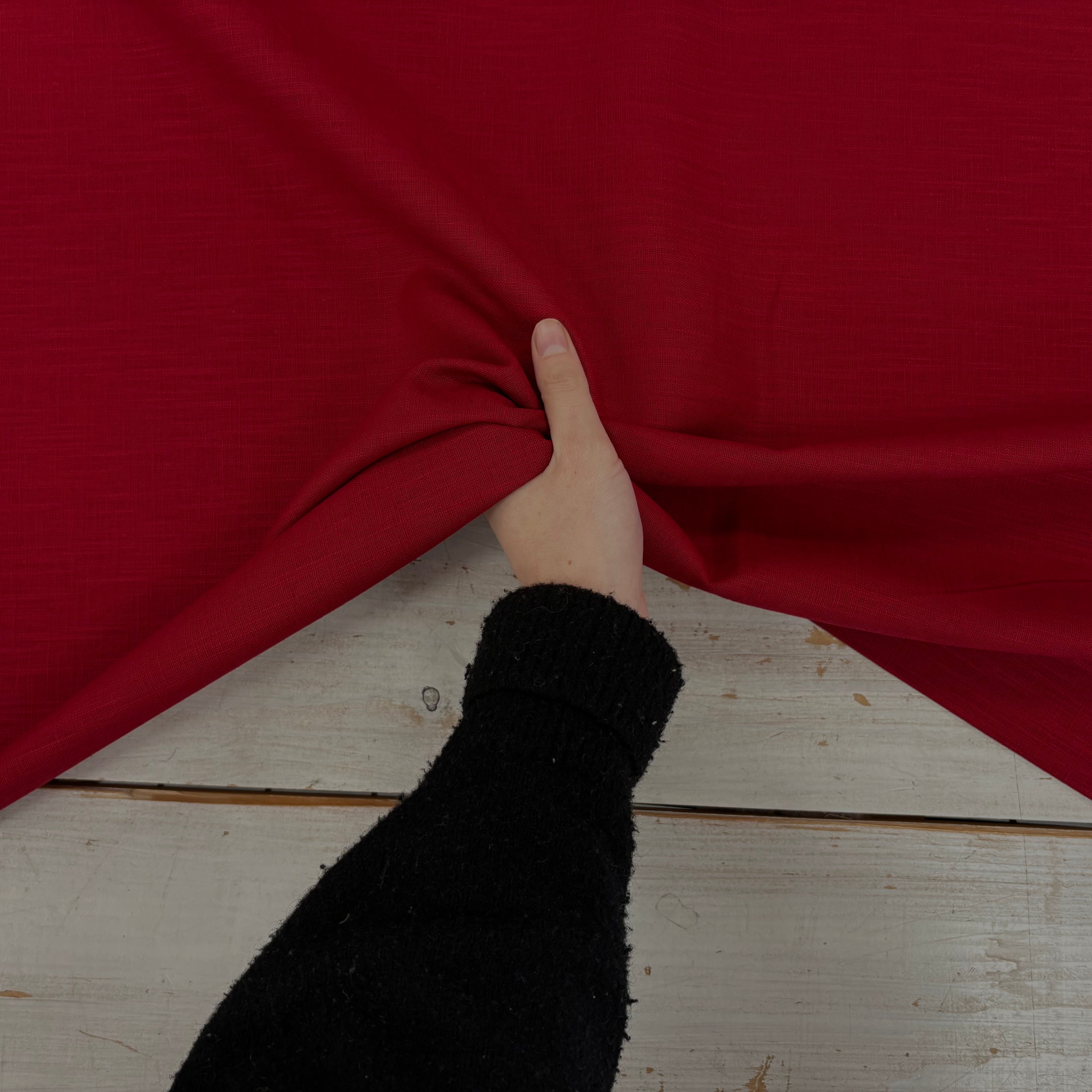 Red ramie linen dress fabric with a natural woven texture being held to show movement 