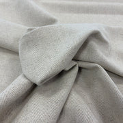 A close-up of draped linen with a subtle herringbone texture, arranged in soft folds.