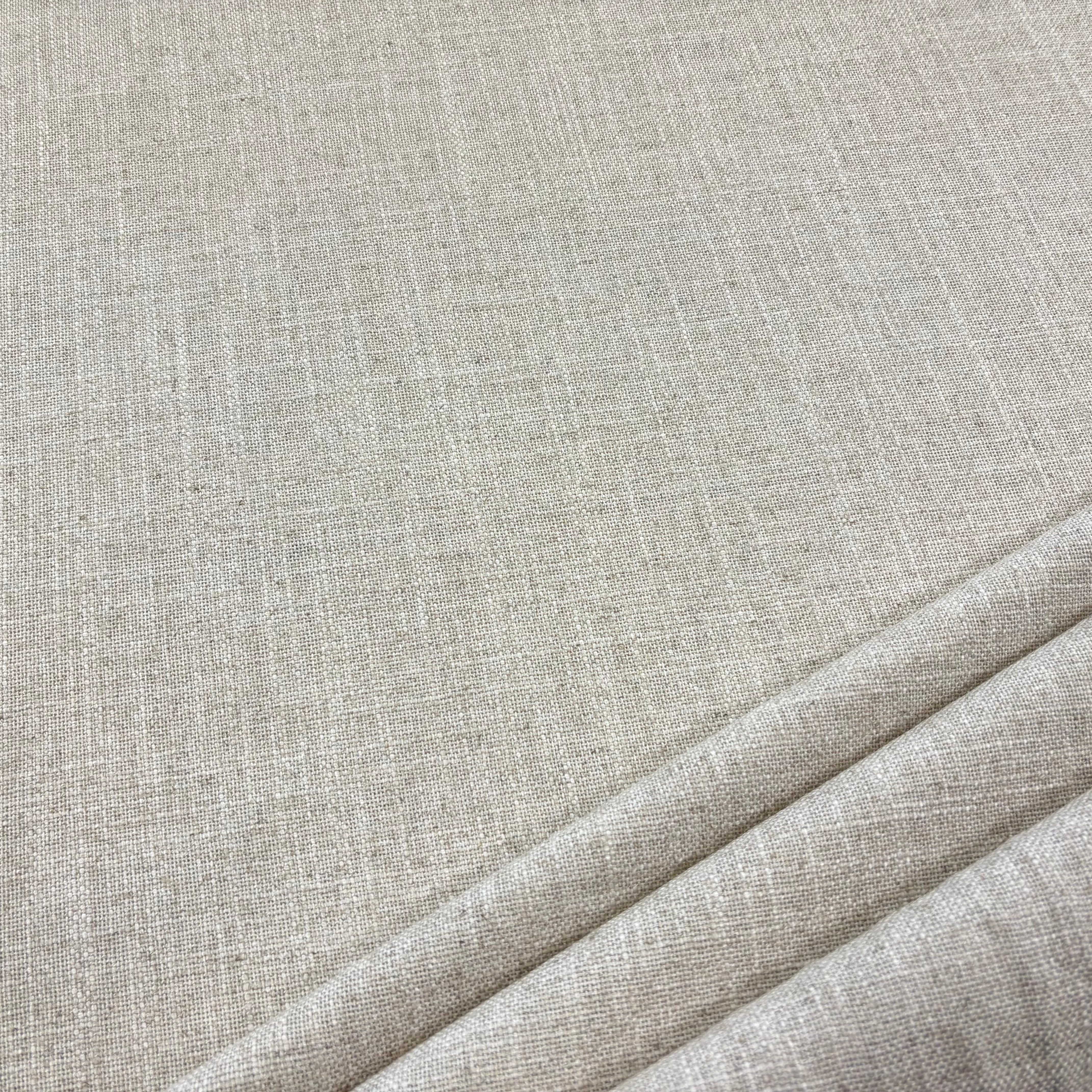 A close-up of light beige woven fabric with a subtle linen-like texture, shown with soft folds in the lower right corner.