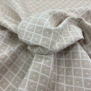 A close-up of draped fabric with a light beige base and diamond weave 