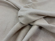 A close-up of draped woven fabric in a light linen tones, showing the texture and pattern of the material.