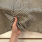 A close-up of a hand holding up a piece of fabric with a black and cream geometric dot pattern, draped over a rustic white wooden surface.