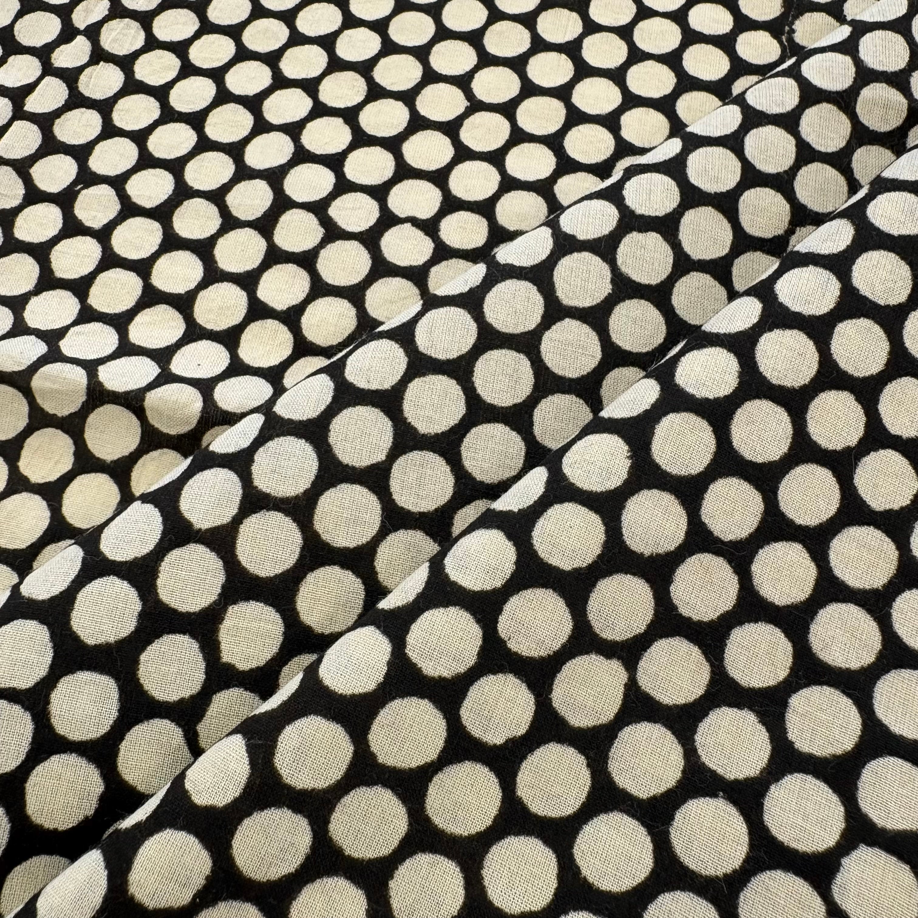 Black fabric with a repeating cream-colored polka dot pattern, shown with soft folds.