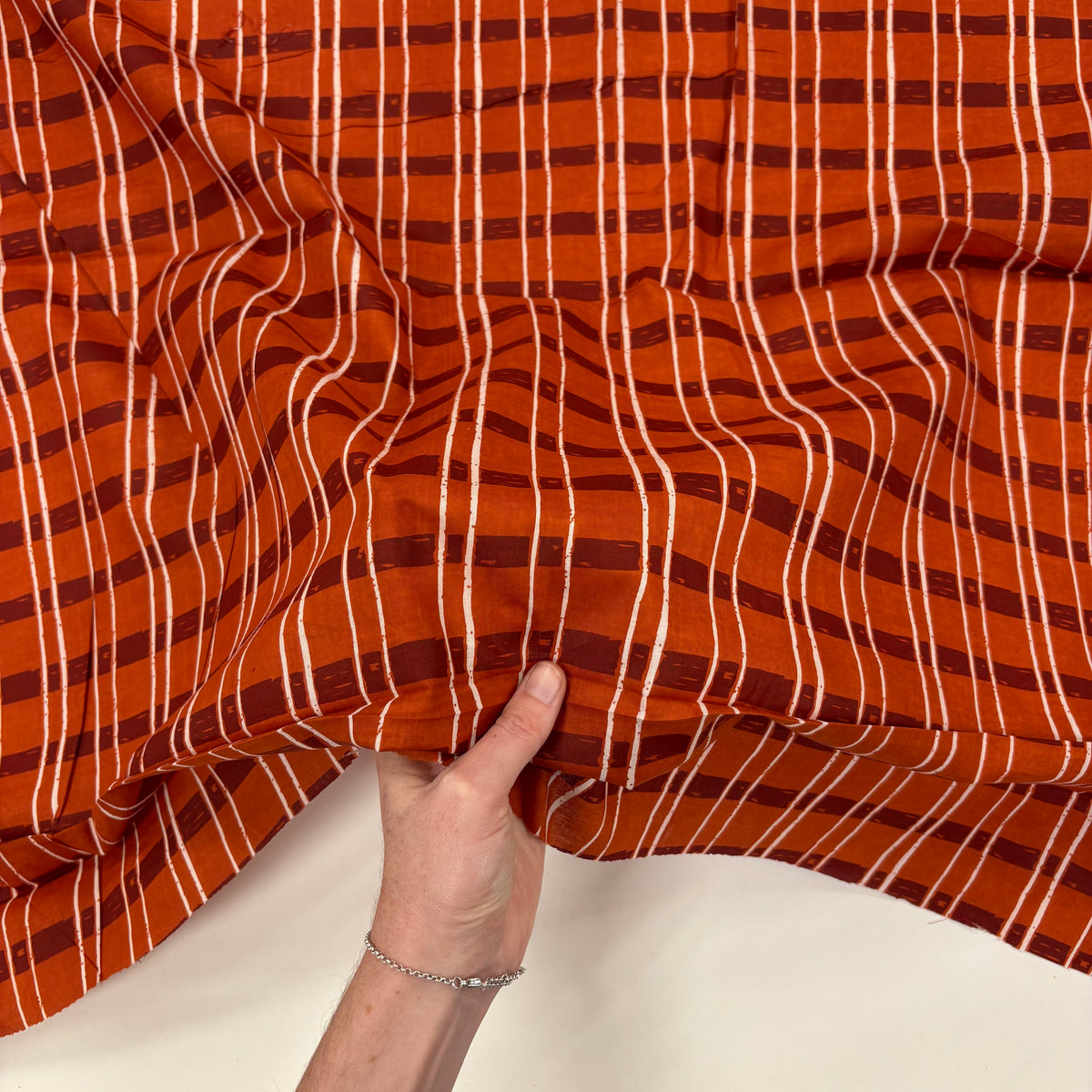 Rust Sketch Tartan Block Print Cotton Fabric, with hand for scale, lightweight soft cotton with a traditional handcrafted Indian tartan check pattern.
