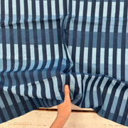 A close-up of a striped fabric with vertical bands of navy, medium blue, and light blue, held up by a hand to show its texture and pattern.