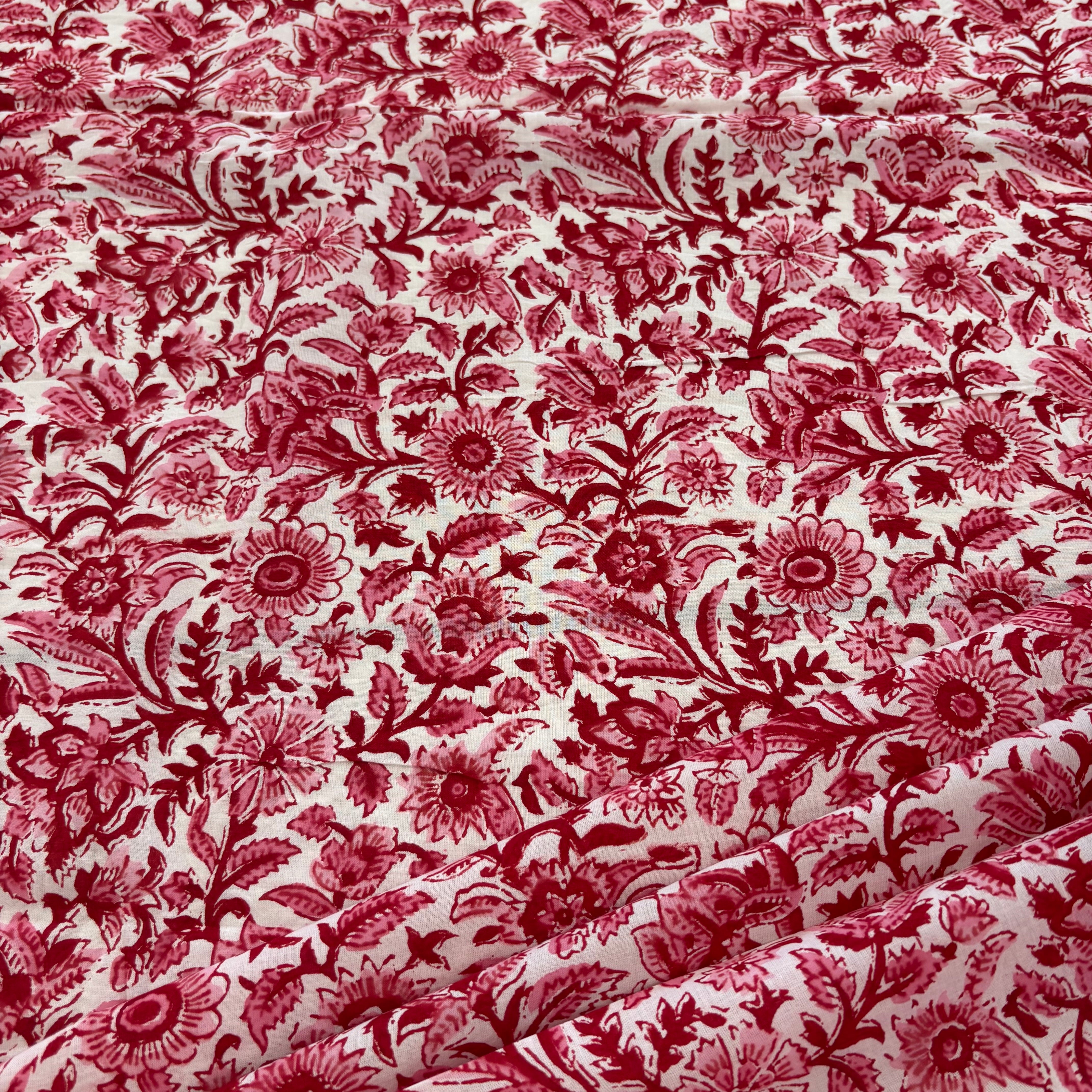 Red floral toile patterned fabric with a white background, draped to show its texture and pattern repeat.