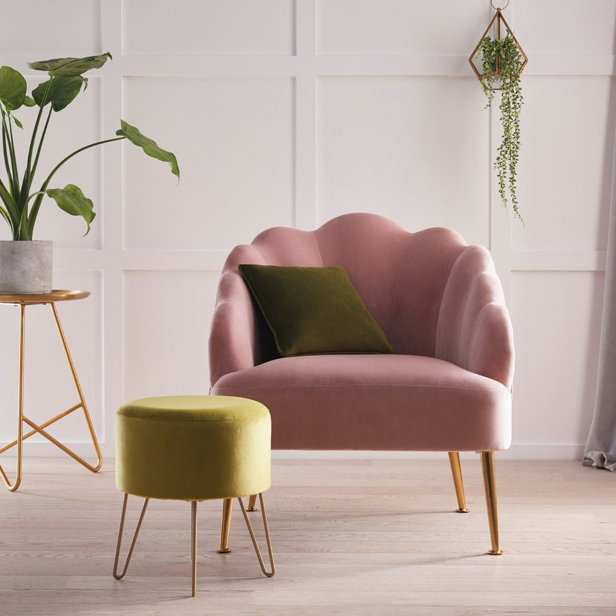 Pink armchair with a green cushion in a room with a plant and small table.