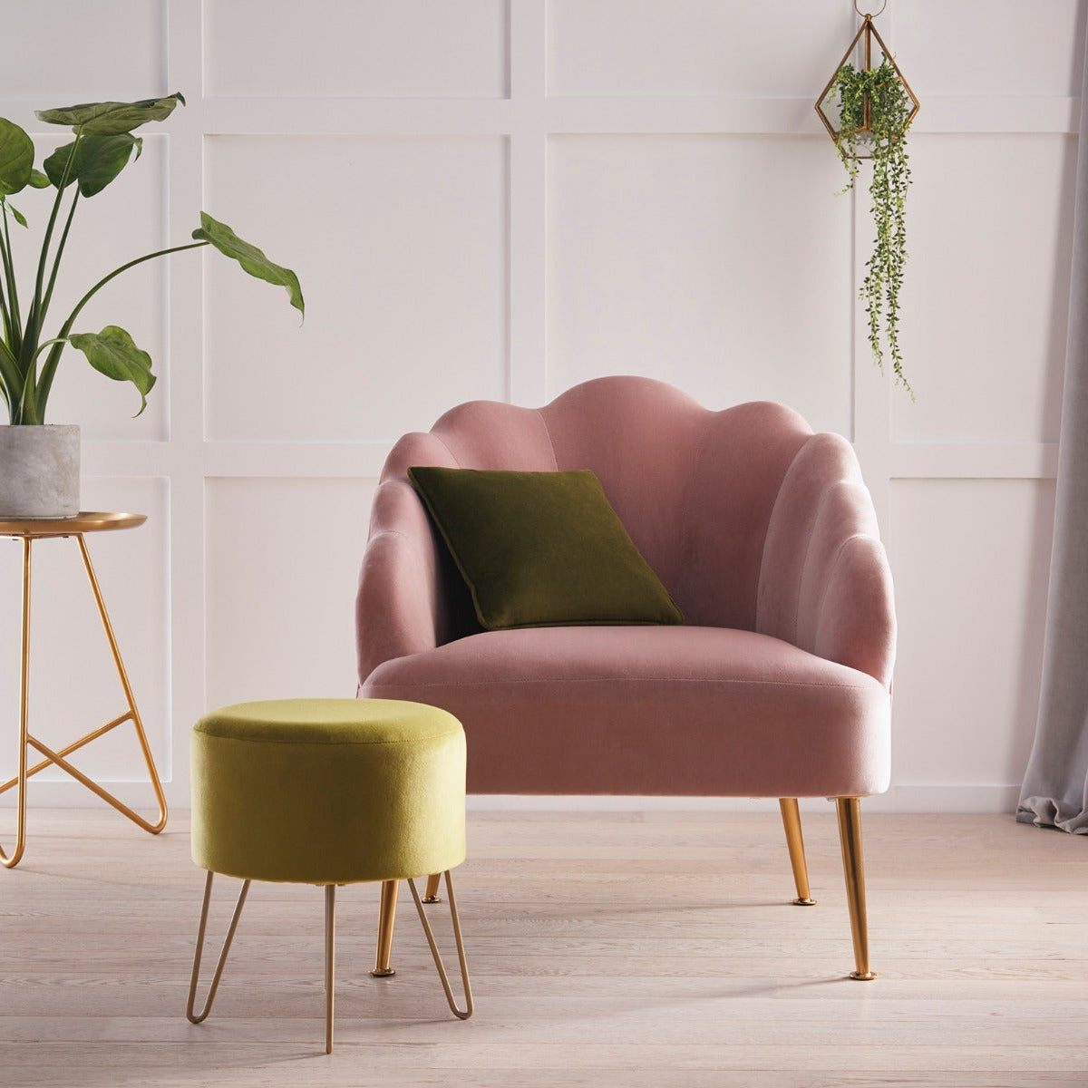 Pink armchair with a green cushion in a room with a plant and small table.