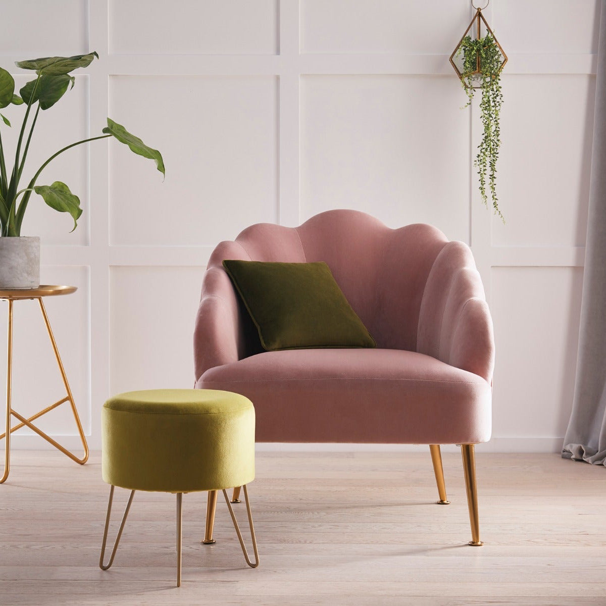 Pink armchair with a green cushion in a room with a plant and small table.