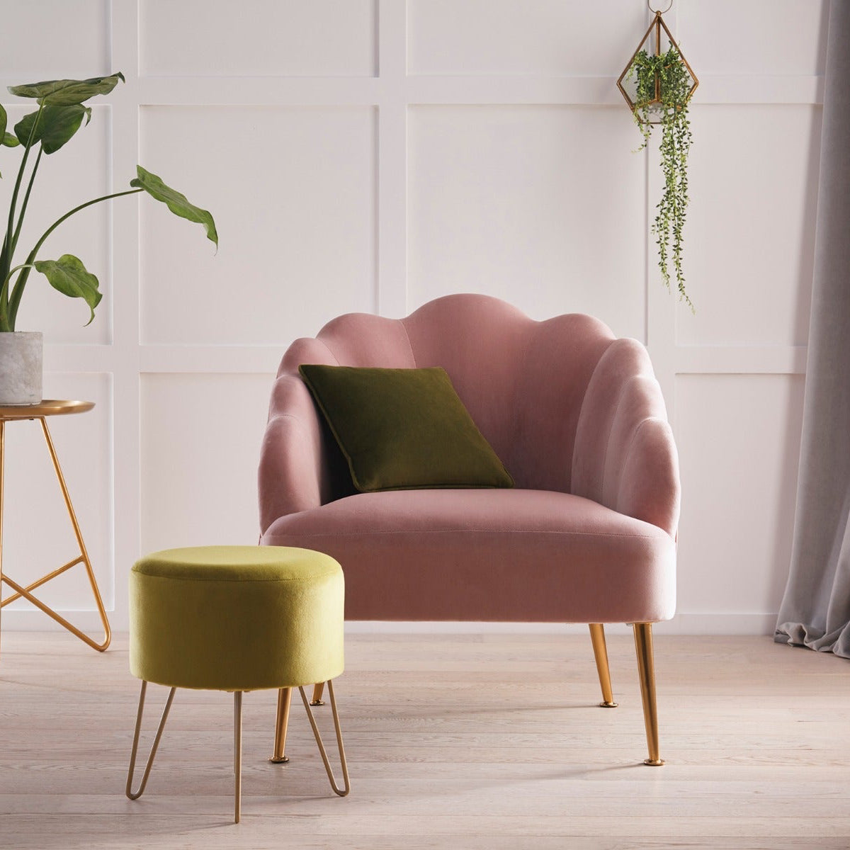 Pink armchair with a green cushion in a room with a plant and small table.