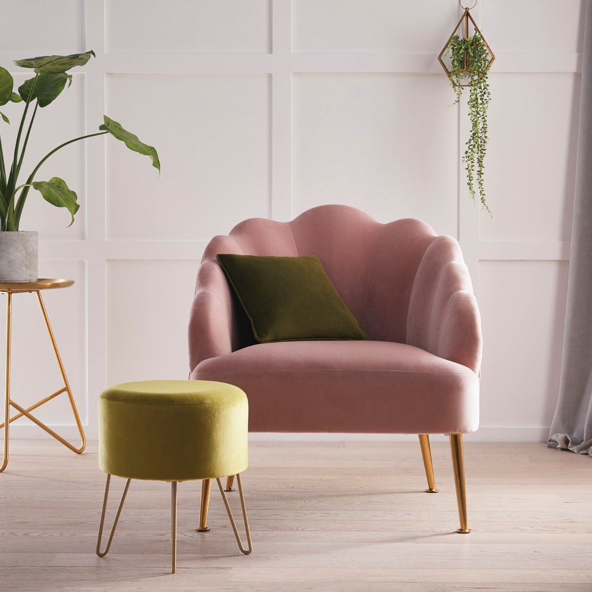 Pink armchair with a green cushion in a room with a plant and small table.