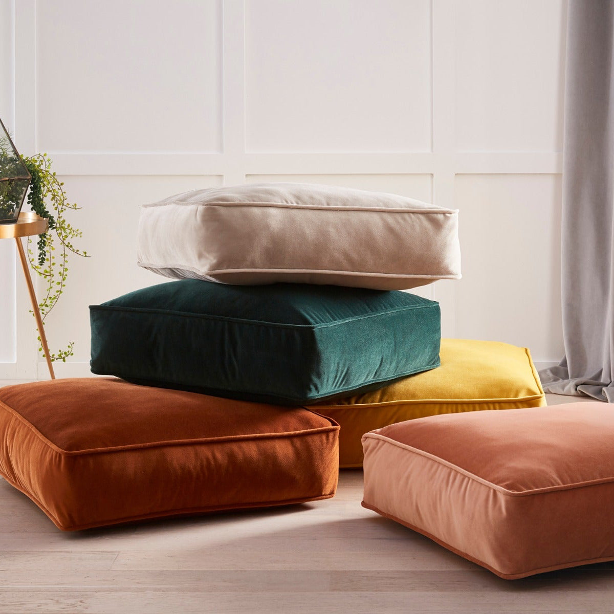 Stack of colorful cushions on a light wooden floor with a neutral wall background