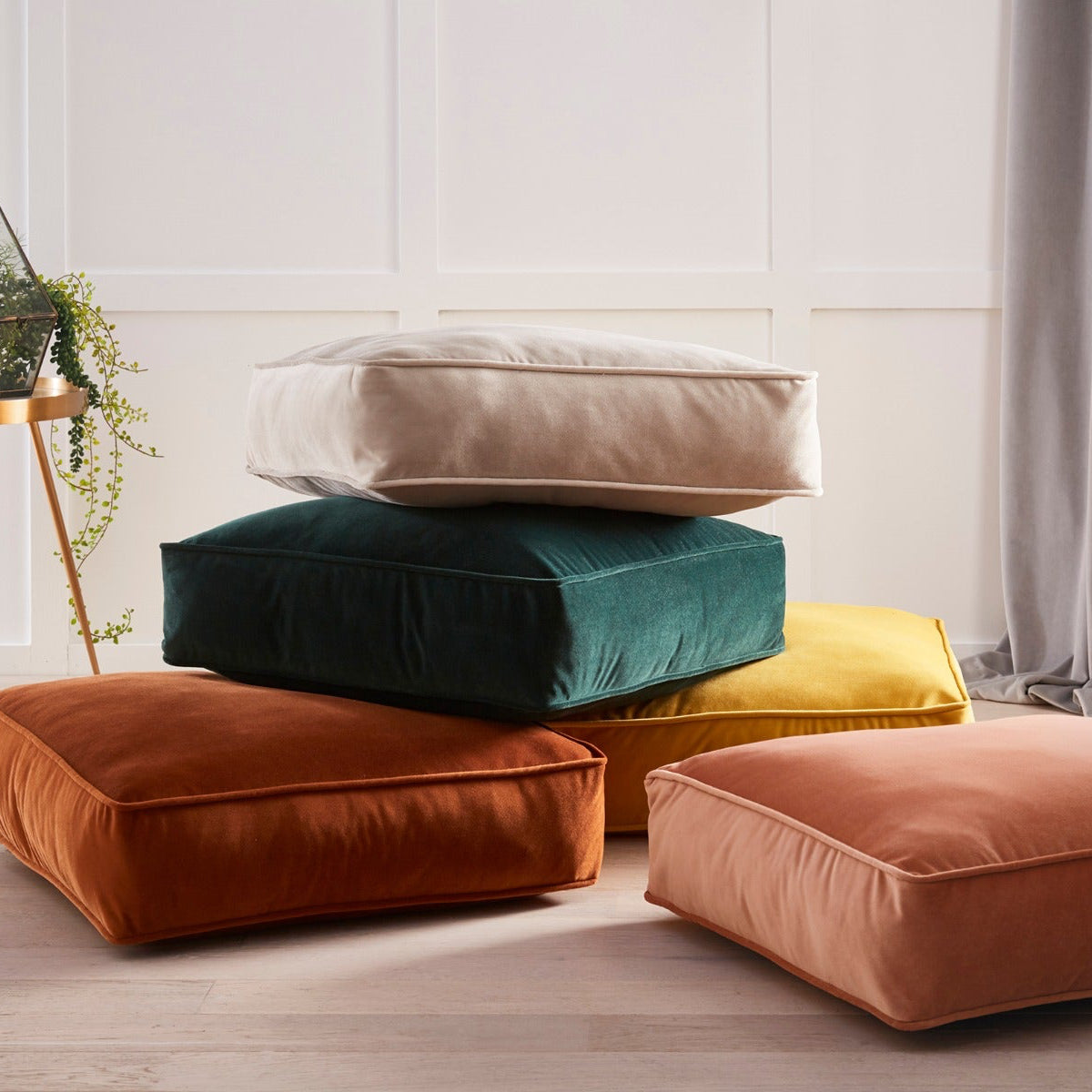 Stack of colorful cushions on a light wooden floor with a neutral wall background
