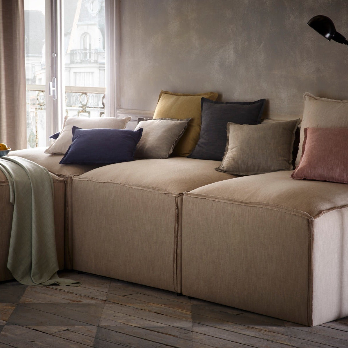 Beige sectional sofa with colorful pillows in a room with large windows.