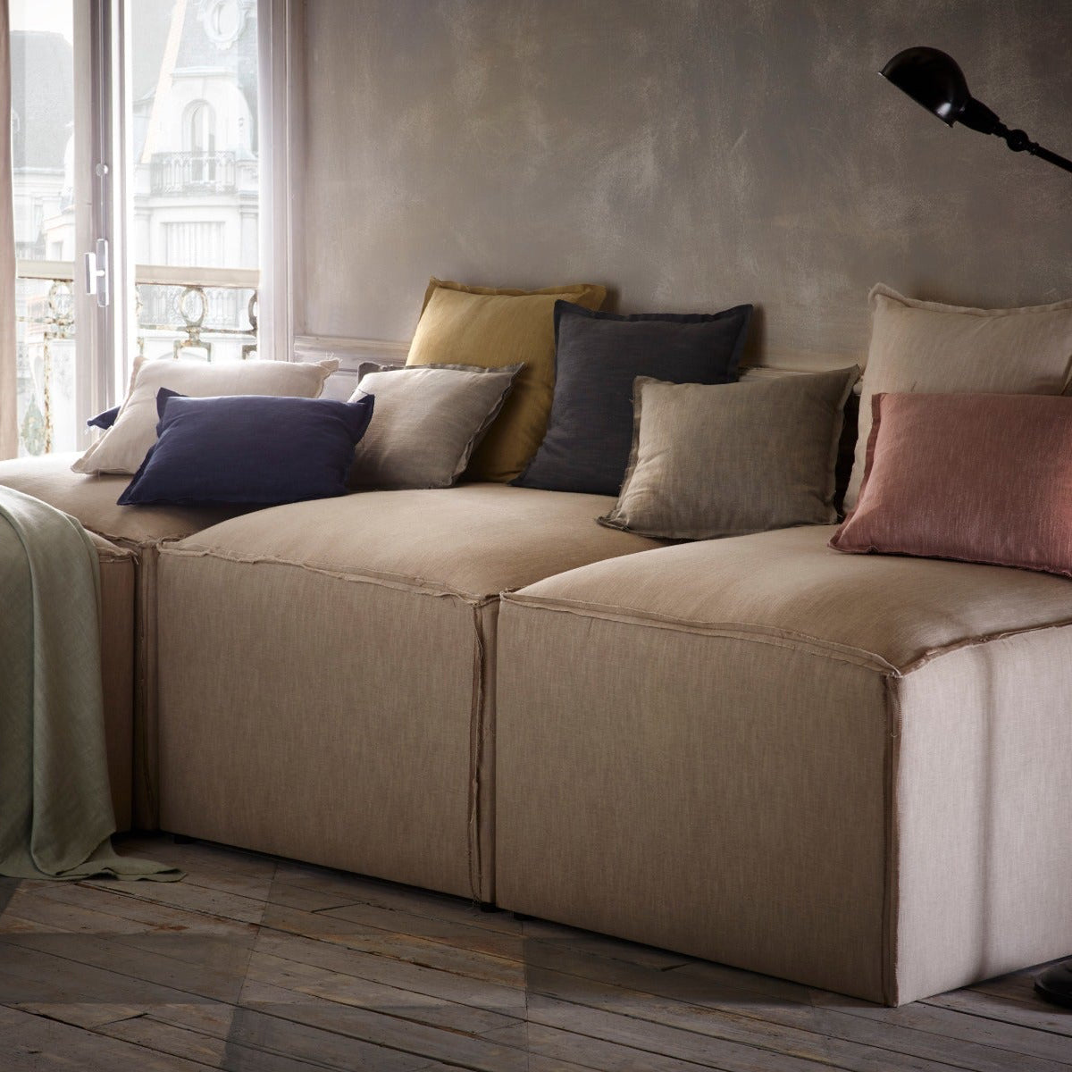 Beige sectional sofa with colorful pillows in a room with large windows.