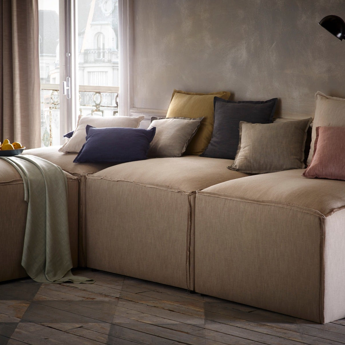 Beige sectional sofa with colorful pillows in a room with large windows.