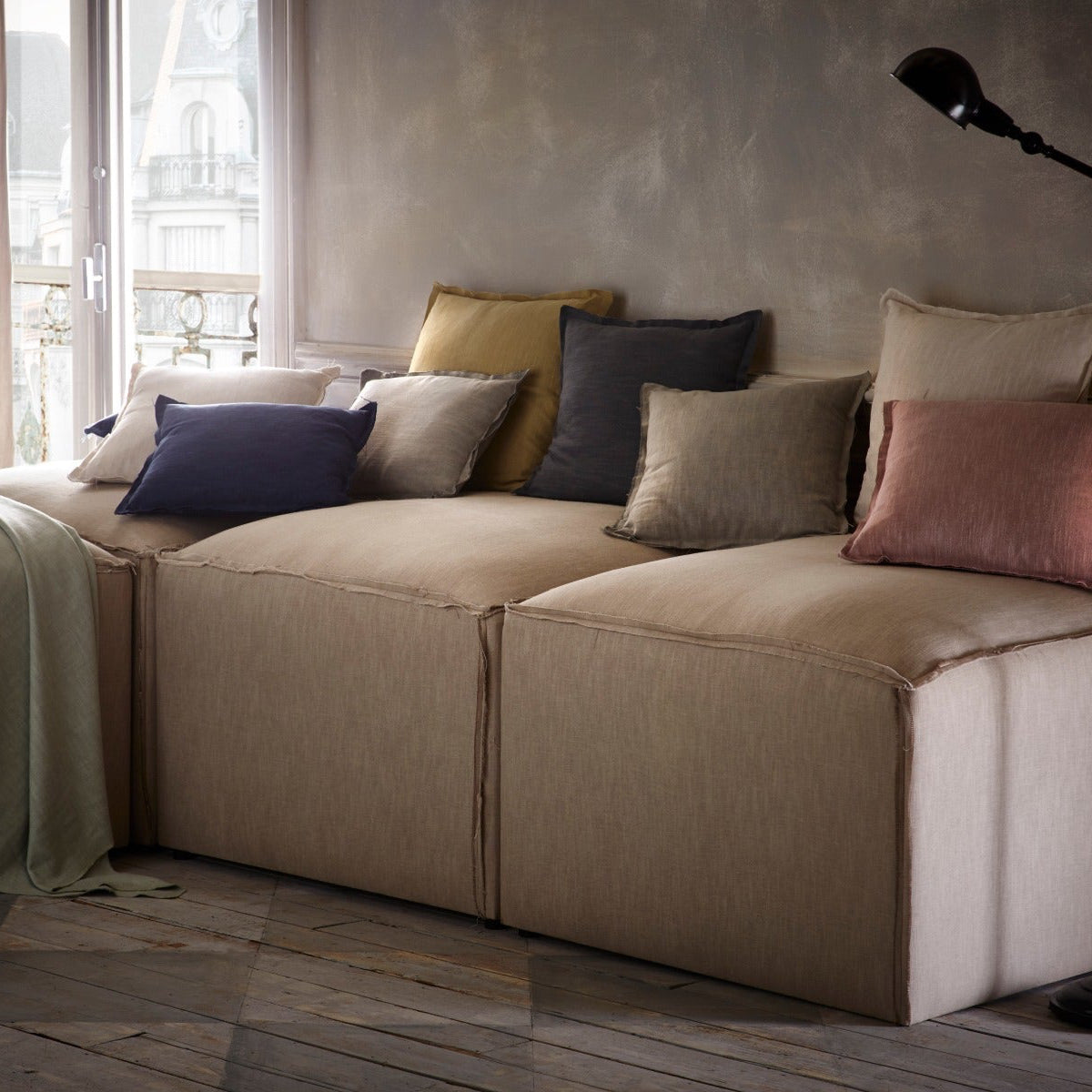 Beige sectional sofa with colorful pillows in a room with large windows.