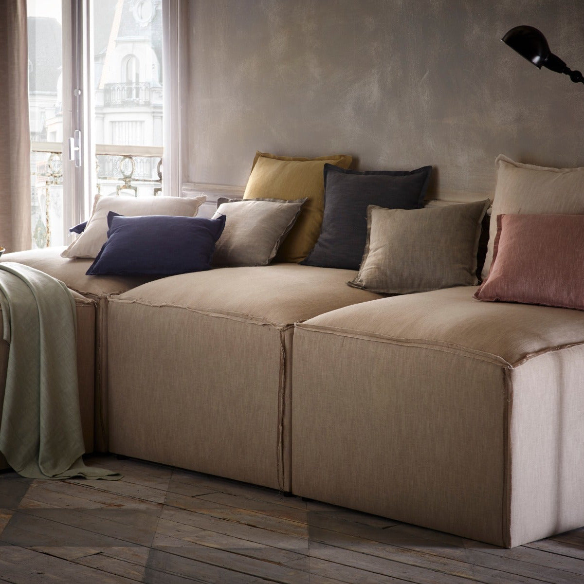 Beige sectional sofa with colorful pillows in a room with large windows.