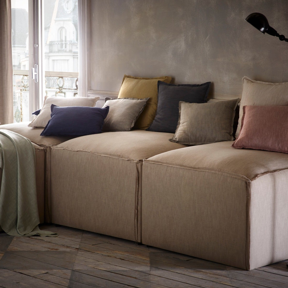 Beige sectional sofa with colorful pillows in a room with large windows.