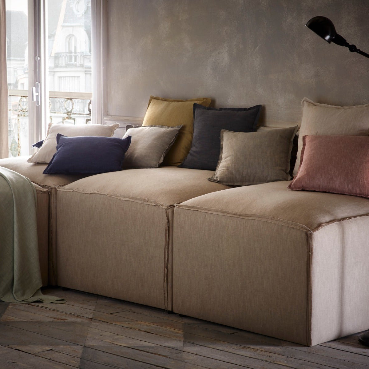 Beige sectional sofa with colorful pillows in a room with large windows.