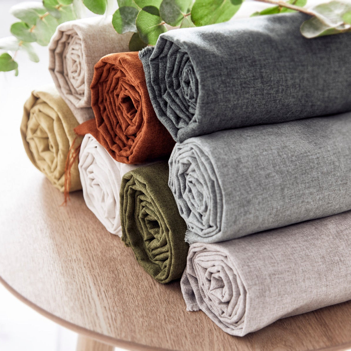 Rolled-up fabric samples in various colors on a wooden surface with greenery in the background